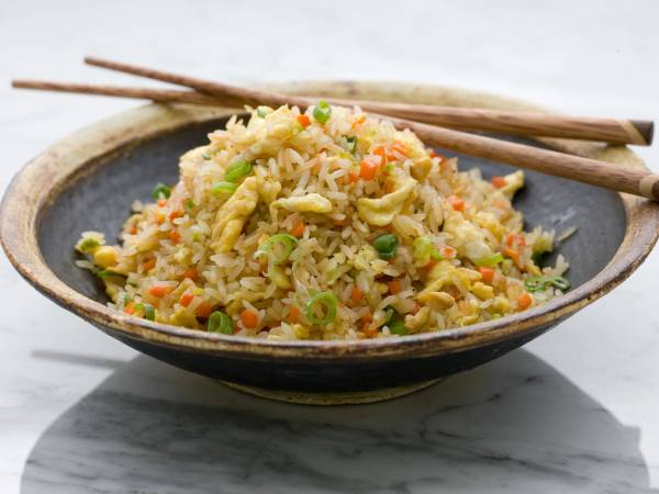 Stekt ris med grønnsaker servert i en svart bolle med spisepinner oppå.
