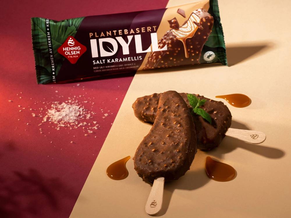 To plantebaserte iskrembarer med sjokoladesmak, pyntet med mynteblad og karamellsaus, plassert på et hvitt underlag.