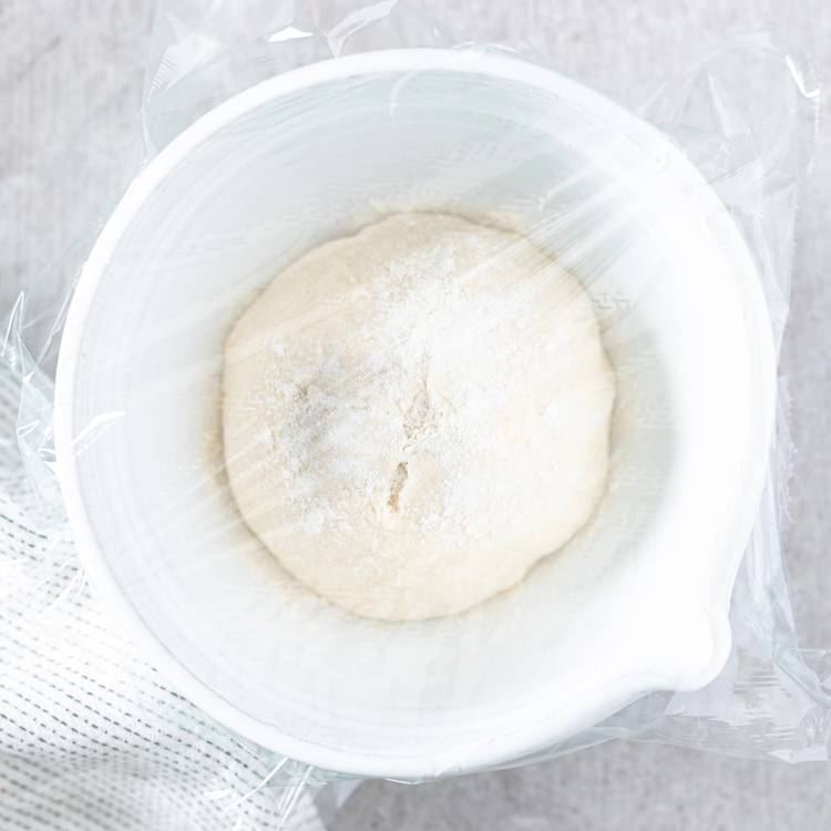 Pizzadeig i en hvit bolle, klar til å bli utkjevlet eller formet, sett ovenfra.