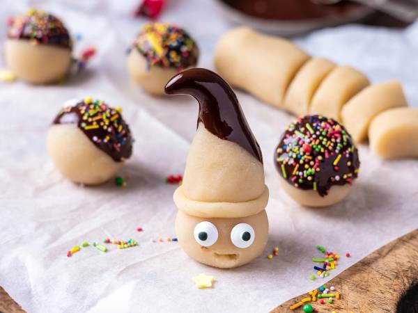 Julemarsipan med sjokoladetrekk og fargerike strøssel, med en marsipanskall som har øyne og en sjokoladestilk som ligner en nisselue, på bakepapir.