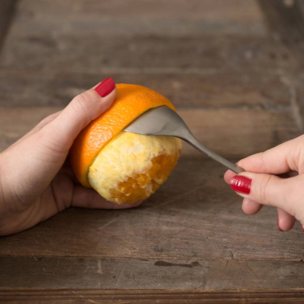 En person skreller en klementin med en kniv over et trebord.