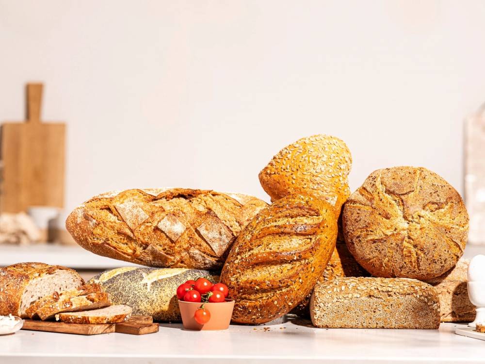Ulike typer brød og bakverk på et bord med en liten bolle med cherrytomater foran.