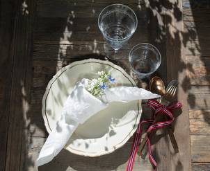 Et festbord med en hvit serviett med blomster, en tallerken, et glass vann og bestikk med norsk flaggbånd, klar for 17. mai-feiring.