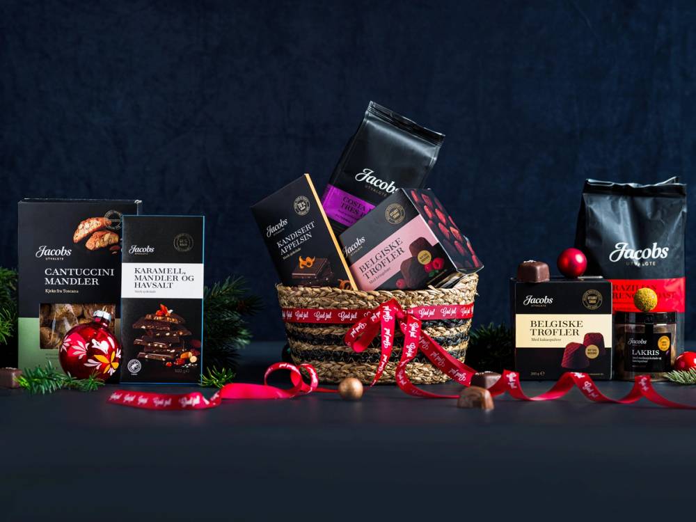 Ulike sjokoladegaver pakket inn med julebånd og pynt, plassert på en mørk bakgrunn.