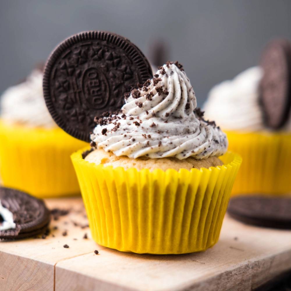 En cupcake med oreo-krem og et halvt oreo-kjeks på toppen i en gul papirform, omgitt av flere lignende cupcakes.