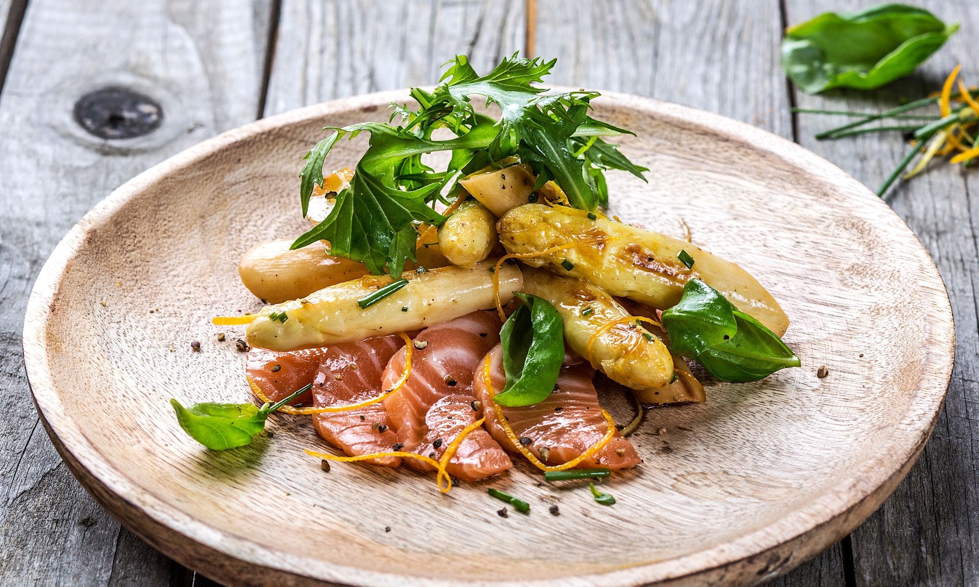 Smørstekte hvite asparges med laks, sitrus og frisk grønn salat på en beige tallerken.