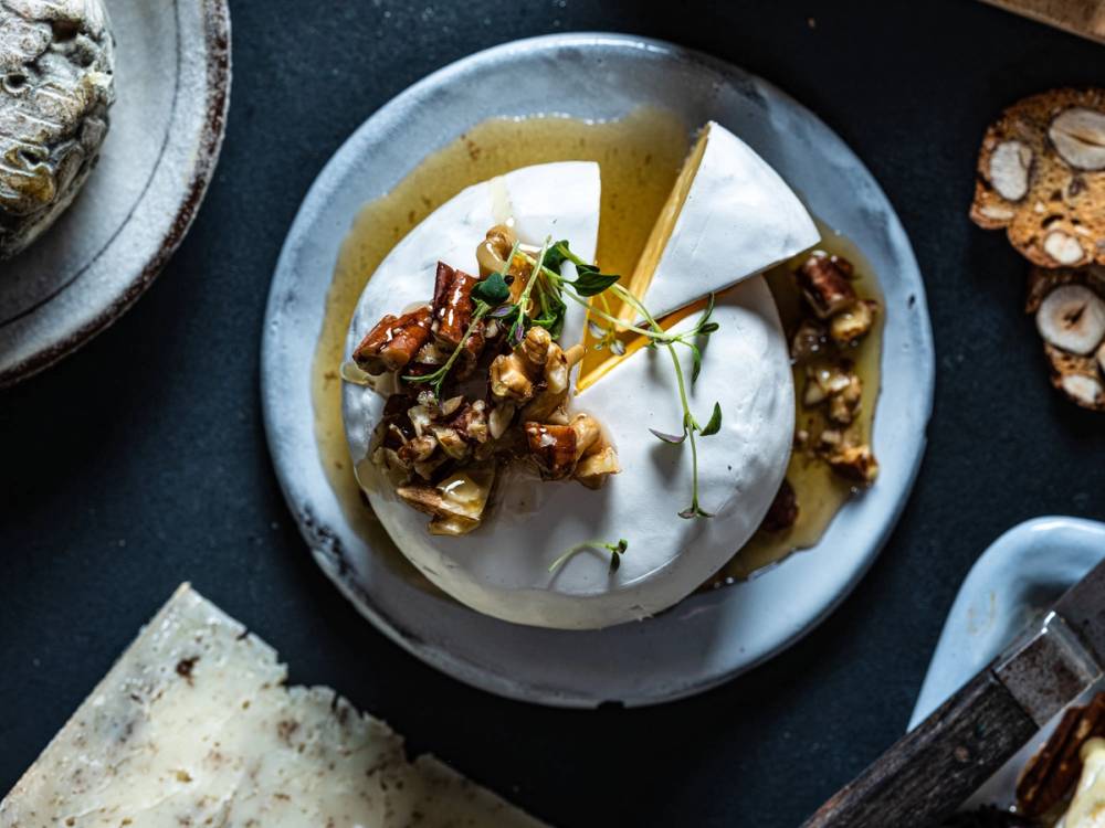 Et ostefat med ulike oster, nøtter og urter på en tallerken.