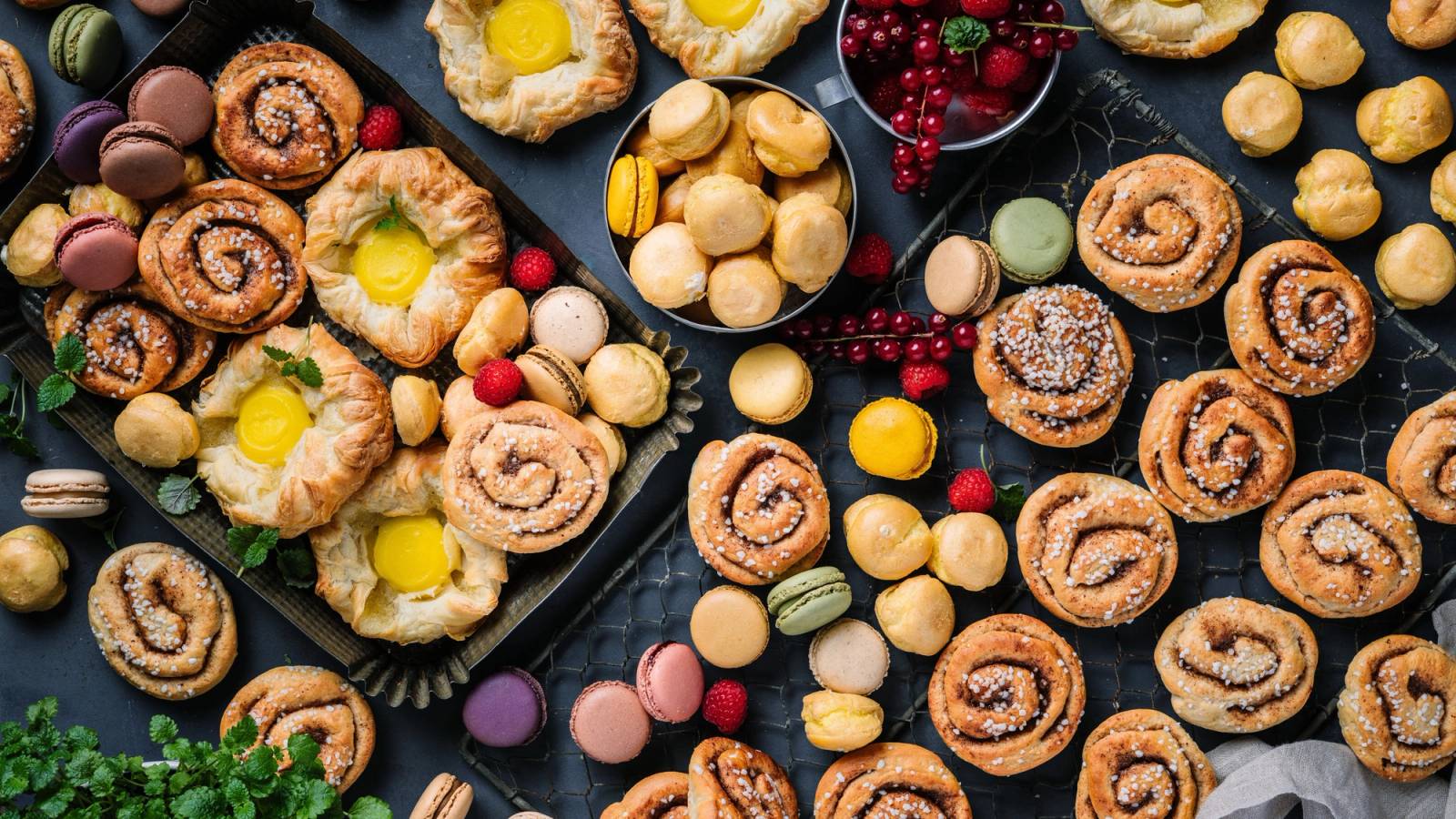 Ulike småbakst og kaker på en svart bakgrunn, inkludert kjeks, småkaker og godteri.