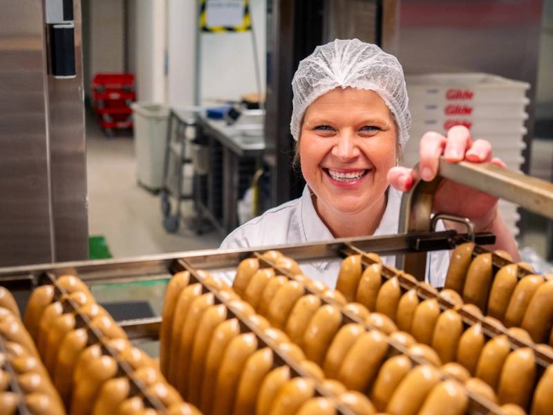 Person i hvit kjeledress og hårnet inspiserer egg på en produksjonslinje i et bakeri eller matfabrikk.