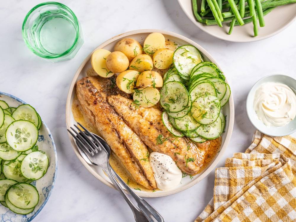 Stekt makrell med agurksalat og poteter servert på et hvitt fat med tilbehør som rømme og agurkskiver på siden.