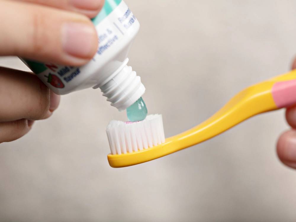 En person som presser ut tannkrem fra en tube på en tannbørste, med en tannkremindikator på tuben synlig i bildet.