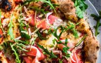 En pizza med skinke, ruccola og ost på en hvit tallerken.