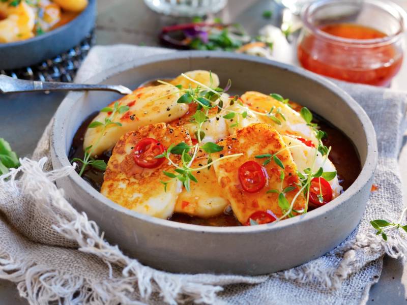 Stekt halloumi med cherrytomater og urter på en tallerken, med en liten skål med tomatsaus i bakgrunnen.
