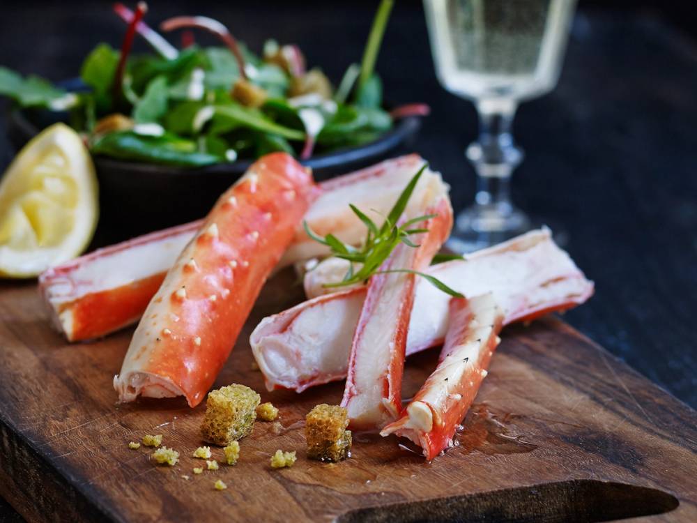 Kokt kongekrabbe med dressing og sitron på et serveringsfat, med et glass vin i bakgrunnen.