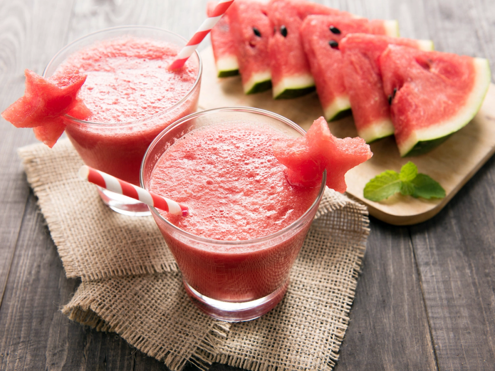 To glass med vannmelonjuice og flere skiver vannmelon med mynte på et trebrett