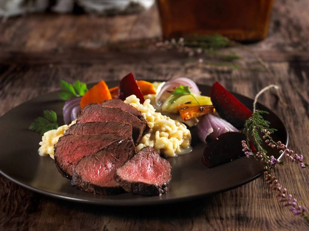 Hjortefilet servert med risotto og grønnsaker på en svart tallerken