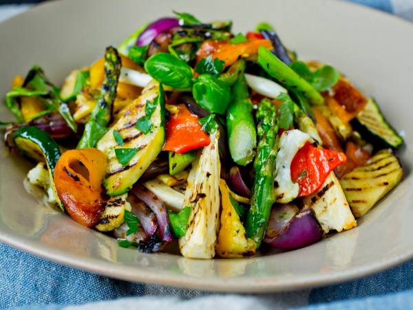 Grillet grønnsakssalat med paprika, squash, rødløk og basilikum på en tallerken.