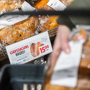 Gårdagens brød i butikkhyllen med en prisetikett som viser 15 kroner, og en person som holder en brødpose i hånden.