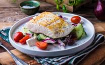 Stekt kveite servert med gresk salat med cherrytomater, agurk og rødløk på en hvit tallerken.