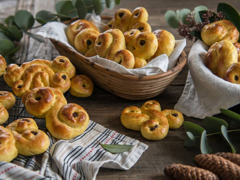 Bak-lussekatter med rosiner i en kurv og på et bord, klare til Lucia-feiring.