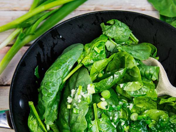 Frisk spinat i en svart bolle med noen grønne vårløk i bakgrunnen