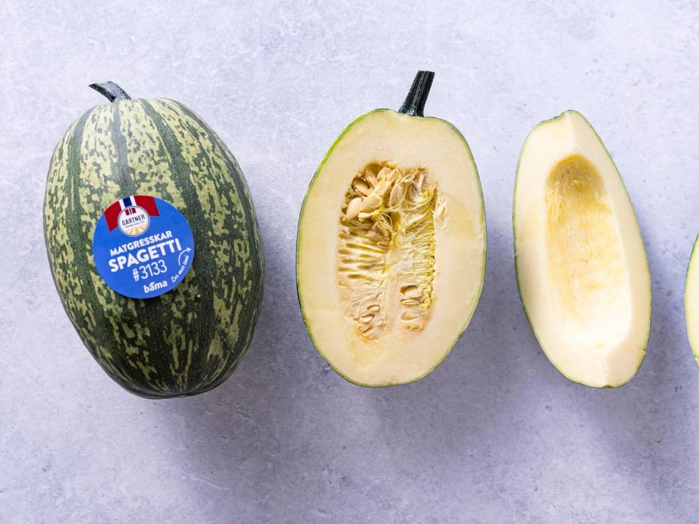 Et spagettigresskar som er delt i to, med frø og innmat synlig, plassert på en lys bakgrunn.