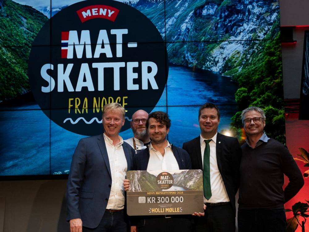 Fire personer holder et stort sjekk med teksten 'KR 300 000' foran en skjerm som viser 'Meny Mat Skatter fra Norge'.
