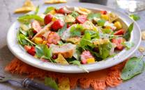 En frisk jordbærsalat med kyllingbiter og grønne blader på en hvit tallerken, med tortilla chips i bakgrunnen.