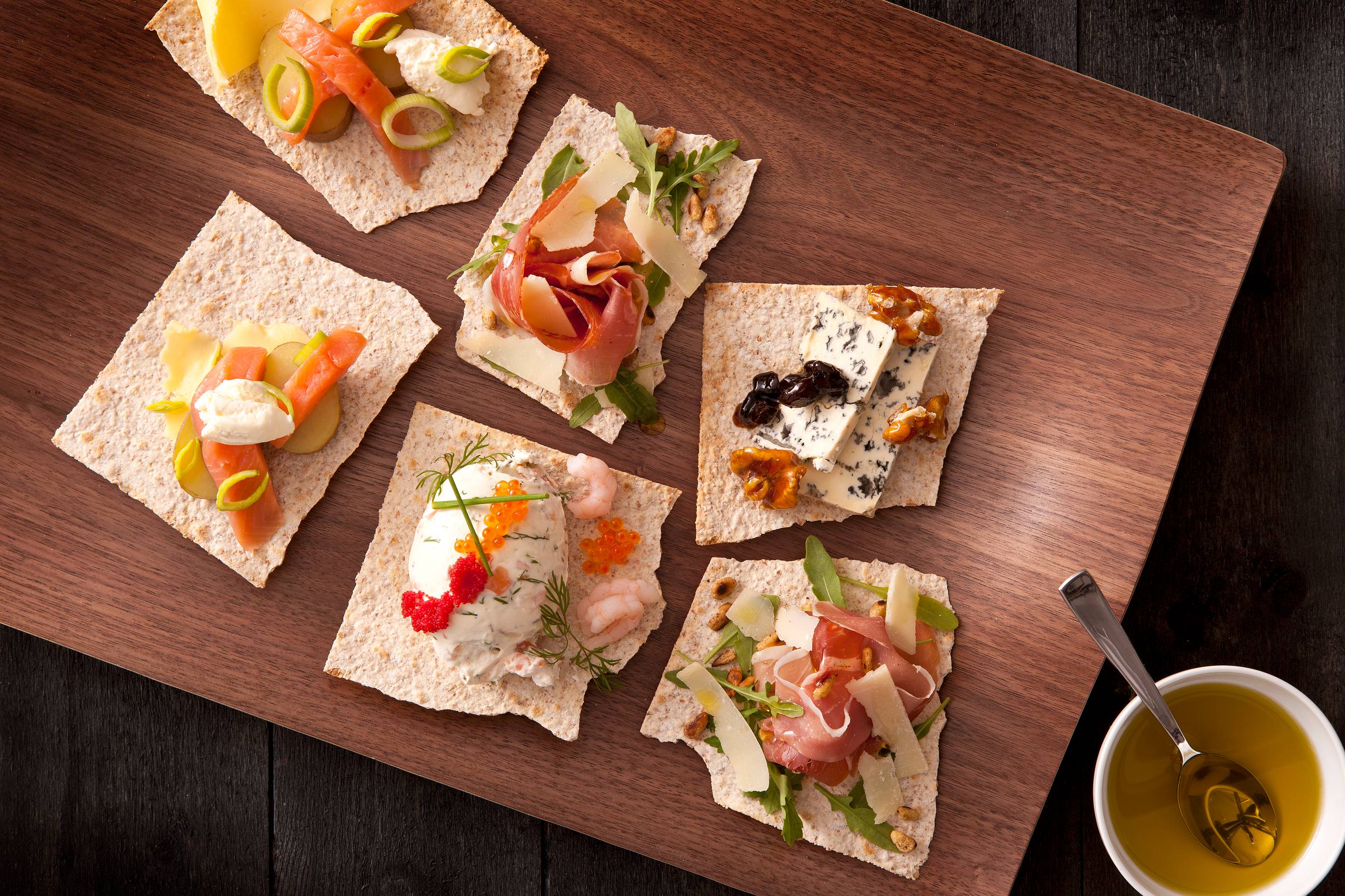 Flatbrød med ulike pålegg som ost, skinke, røkelaks og grønnsaker på et serveringsbrett.