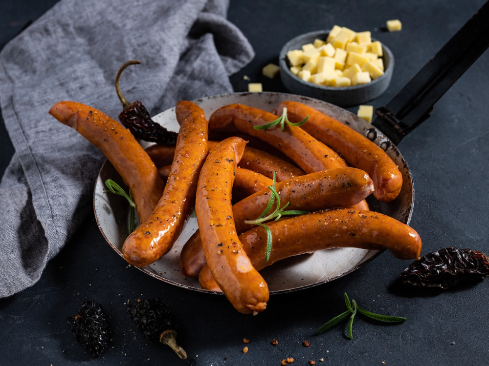 Cheddar- og chipotle-krydret pølse på en svart tallerken med ostebiter og urter rundt.