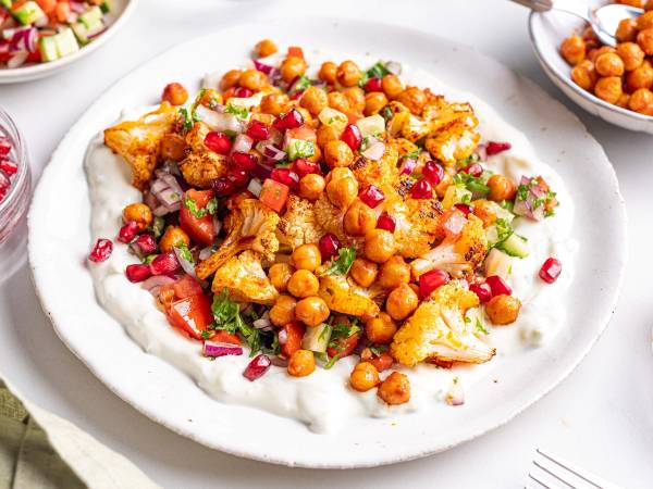 En tallerken med blomkål og kikerter dekket med hakkede grønnsaker og urter, ser ut som en vegetarisk rett.