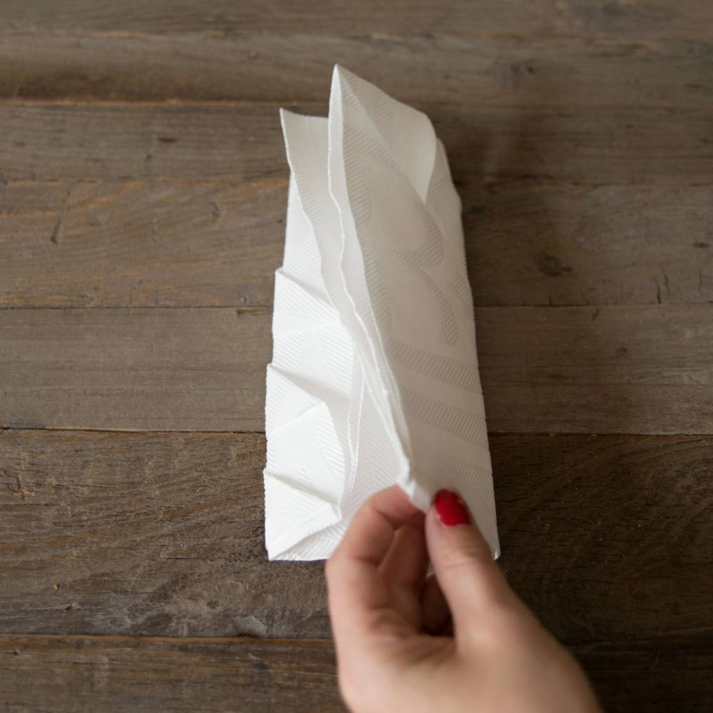 En person holder en brettet hvit serviett over en treflate, klar til bruk til jul.