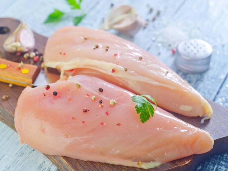 To rå kyllingbryst på en skjærebrett med krydder og urter, klar til å bli tilberedt.