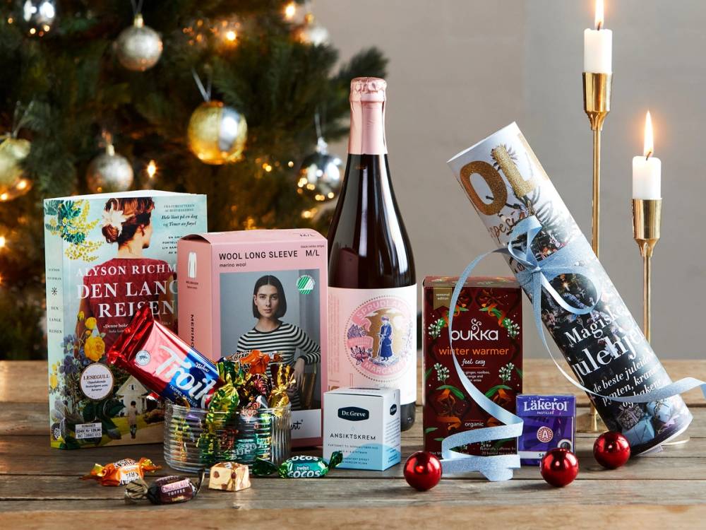 En julekalender med ulike gaver og en flaske med rosévin foran et juletre med pynt og lys.