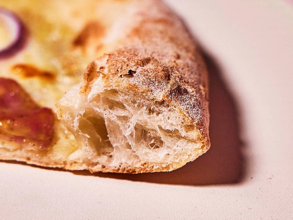 Et stykke pizza med sprø skorpe og ost, som er delvis spist.