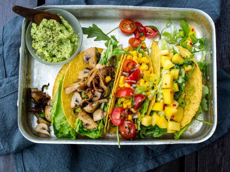 Vegetar-taco fylt med grønnsaker og ost, servert på et fat med en liten skål med guacamole ved siden av.