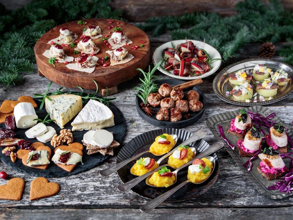Et juletapas-bord med ulike småretter, ost, kjeks, og juledekorasjoner på en treplate og fat.