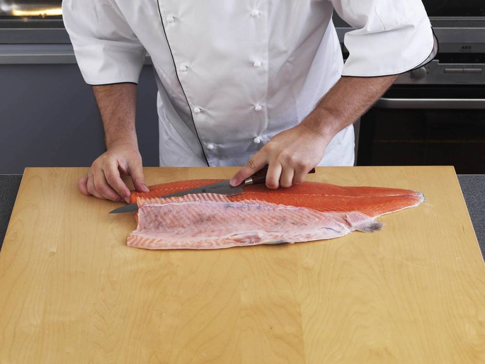 Person som fileterer en hel laksefilet på et kjøkkenbord.