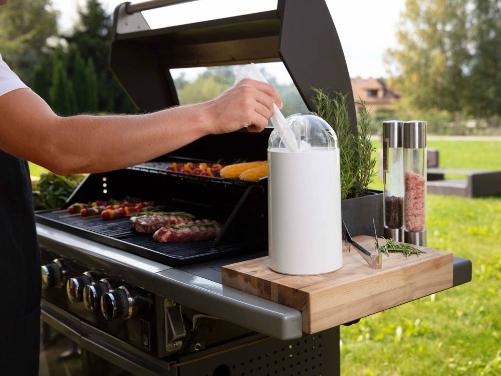 Person som griller kjøtt og grønnsaker på utendørs grill med tilbehør og krydder på en sommerdag.