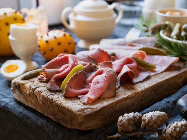 Ulike typer pålegg og skiver av kjøtt på et serveringsbrett til jul, med julepynt og egg i bakgrunnen.