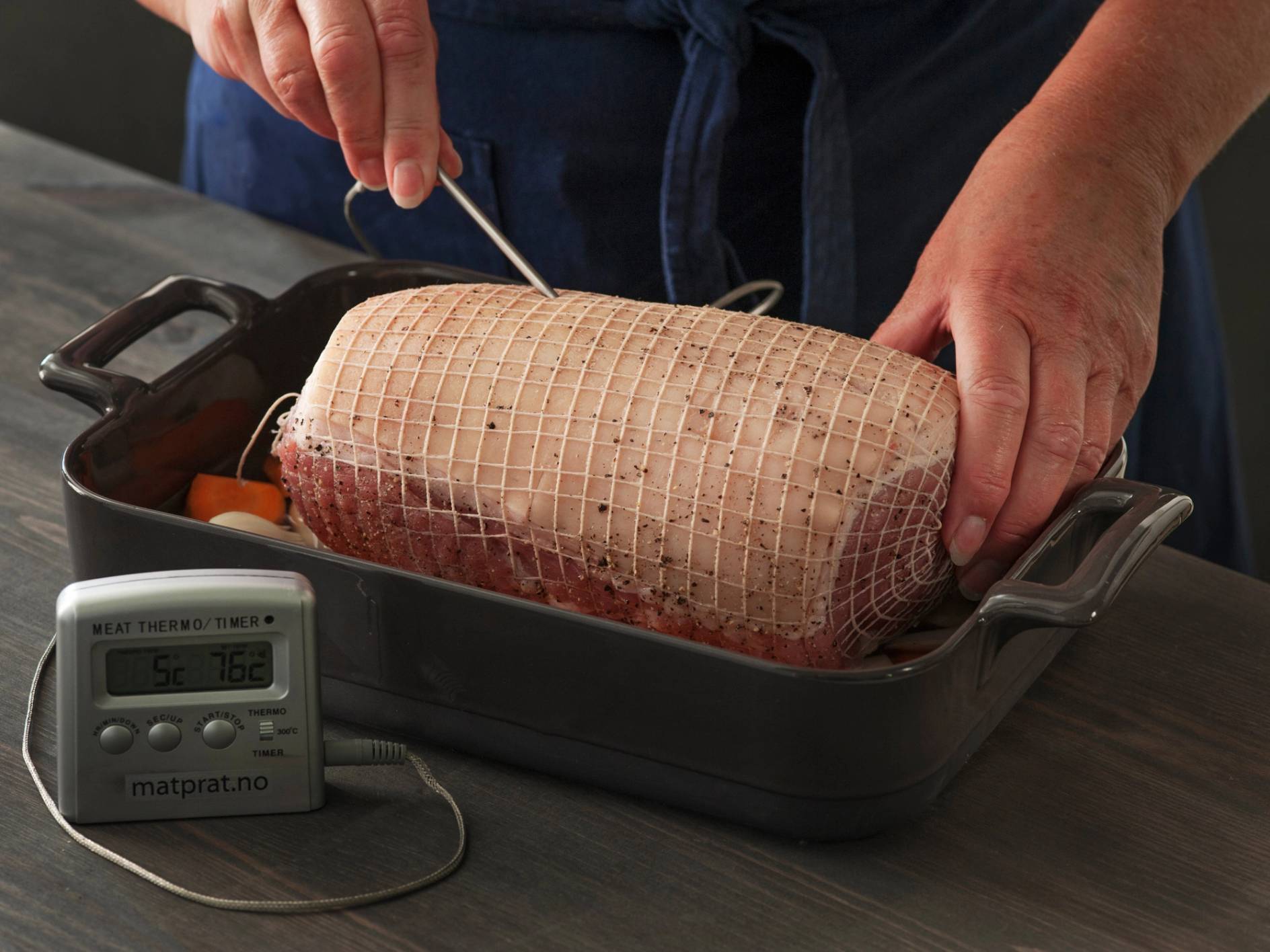 En person som skjærer i en klassisk skinkestek med en kniv i en ildfast form, med en digital steketermometer i nærheten.