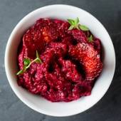 Rødbetepuré i en hvit bolle med noen små grønne urter på toppen.