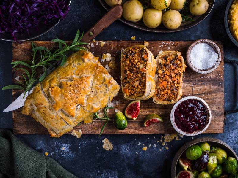 Nøttestek med tilbehør som syltetøy, poteter og grønnsaker på et bord.