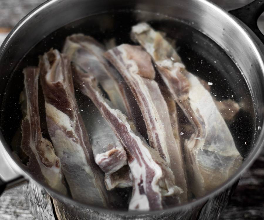 Pinnekjøtt ligger i vann i en stor kjele før koking.