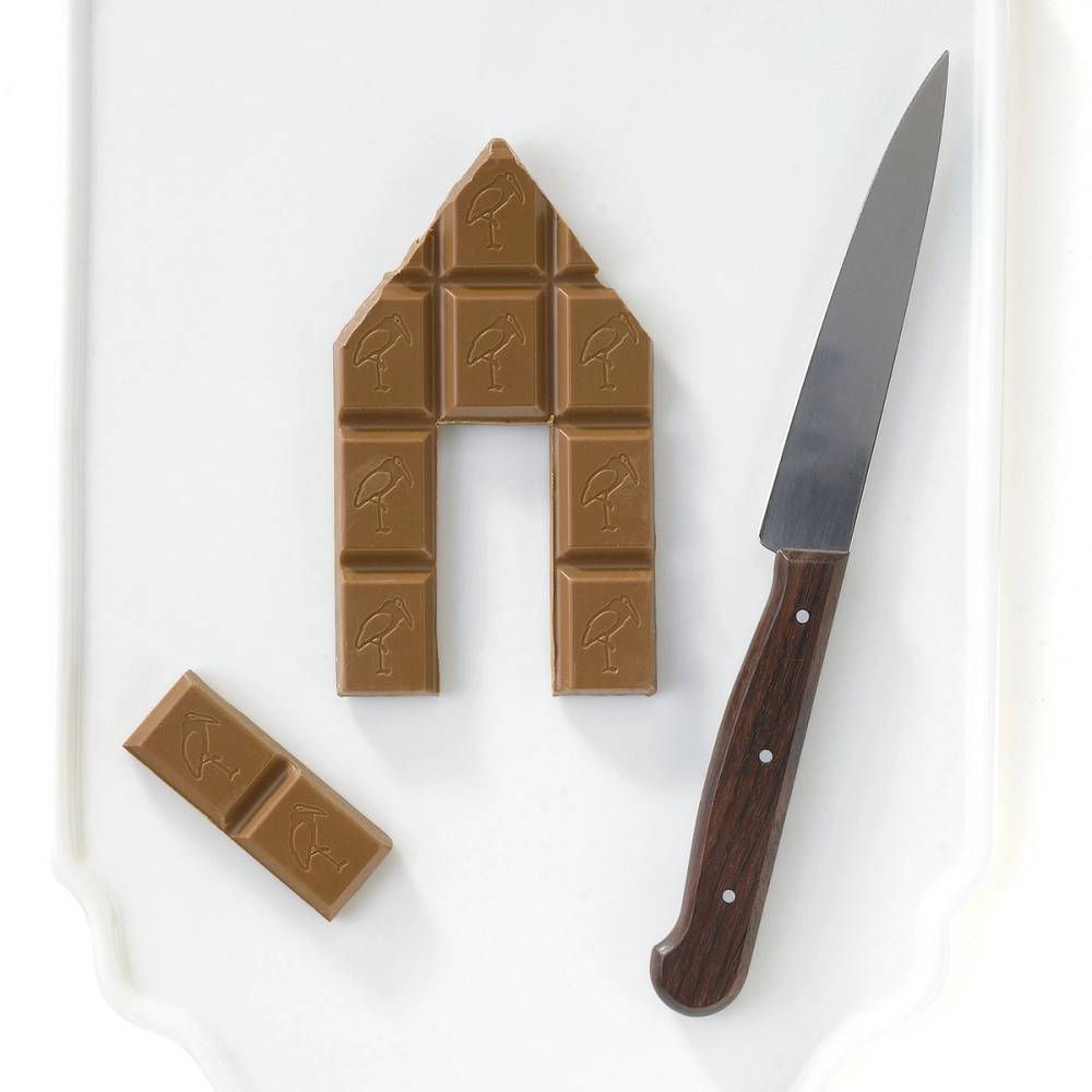 En gruppe med sjokoladestykker formet som et hus på en hvit overflate med en kniv ved siden av.