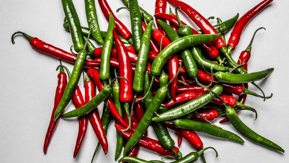 En haug med grønne og røde chilipepper på en hvit bakgrunn