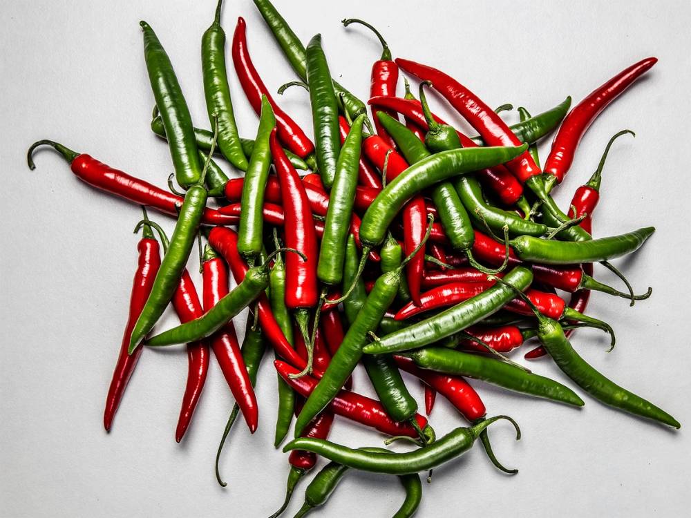 En haug med grønne og røde chilipepper på en hvit bakgrunn