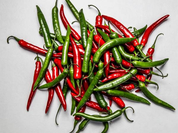 En haug med grønne og røde chilipepper på en hvit bakgrunn