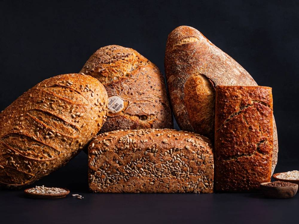 Ulike typer brød på en mørk bakgrunn, inkludert et rundt, et avlange og et firkantet brød med frø og skorpe.
