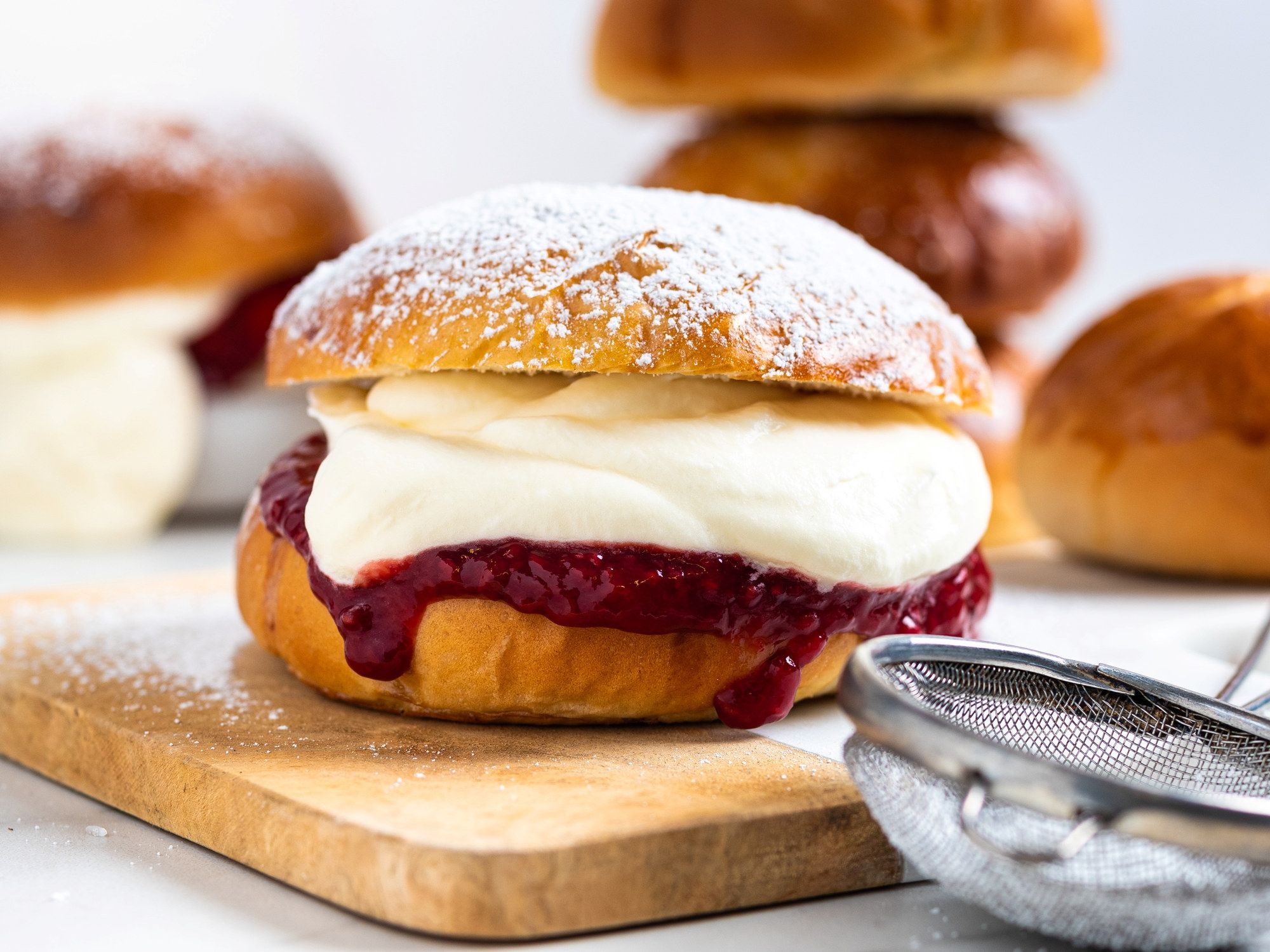 Fastelavnsboller med krem og syltetøy på en skjærefjøl, med flere boller i bakgrunnen.